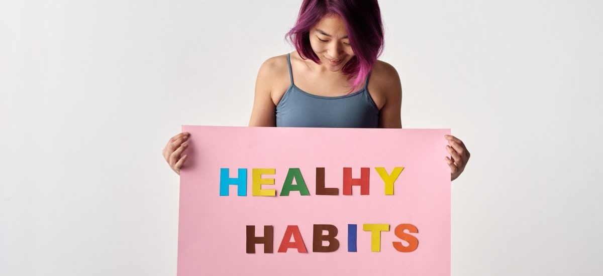 Asian woman holding a colorful 'Healthy Habits' sign in a studio setting, promoting wellness.