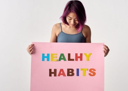 Asian woman holding a colorful 'Healthy Habits' sign in a studio setting, promoting wellness.