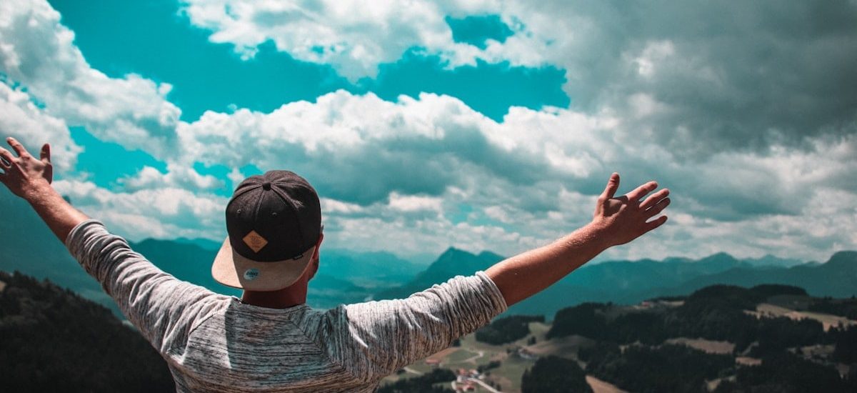 man in grey shirt with black fitted cap raising his hands